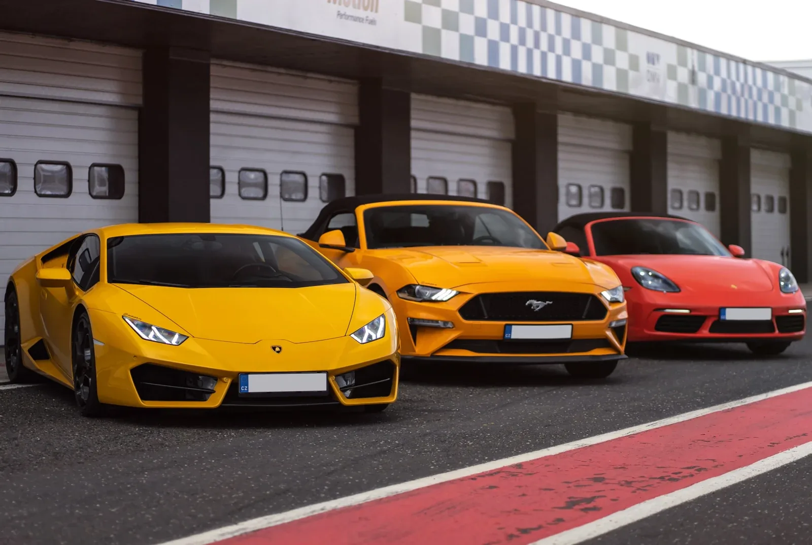 Lamborghini Ford Mustang a Ferrari v boxech závodního okruhu